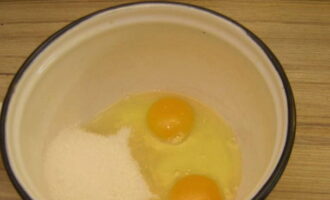 Выбираем подходящий сотейник или кастрюлю для варки крема. Сюда разбиваем куриные яйца и отправляем сахарный песок.