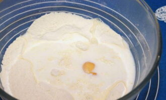 В глубокую миску просеиваем муку, отправляем к ней соль. Перемешиваем сухие продукты, делаем в них ямку и вливаем сюда молоко, разбиваем куриное яйцо.